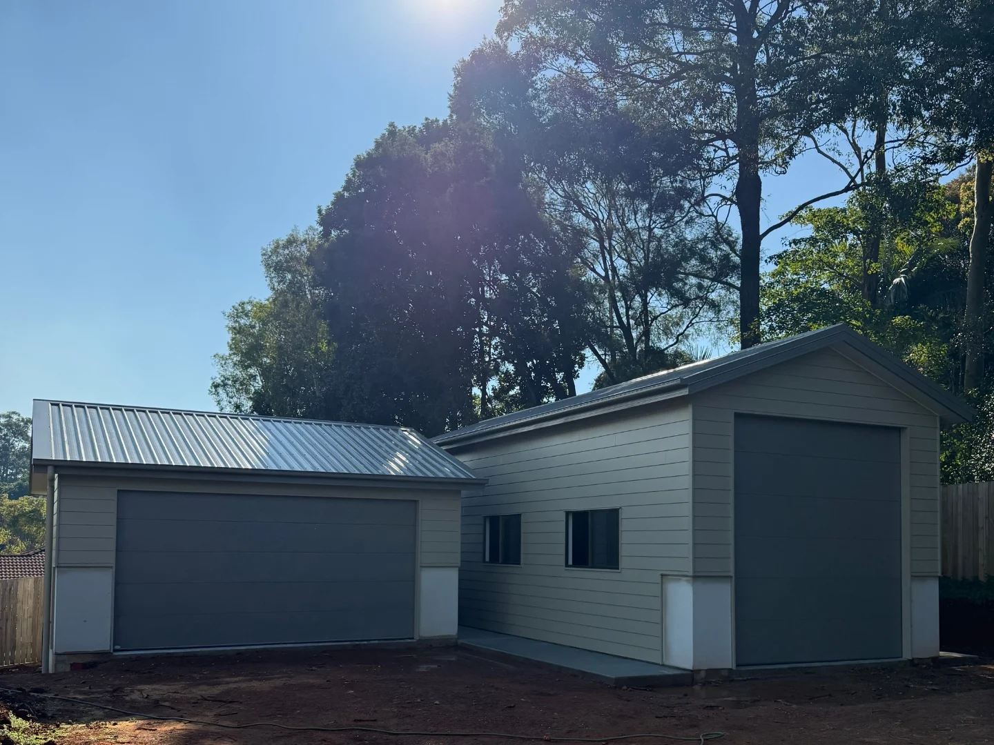 Two separate backyard garages with a metal roof and large doors.