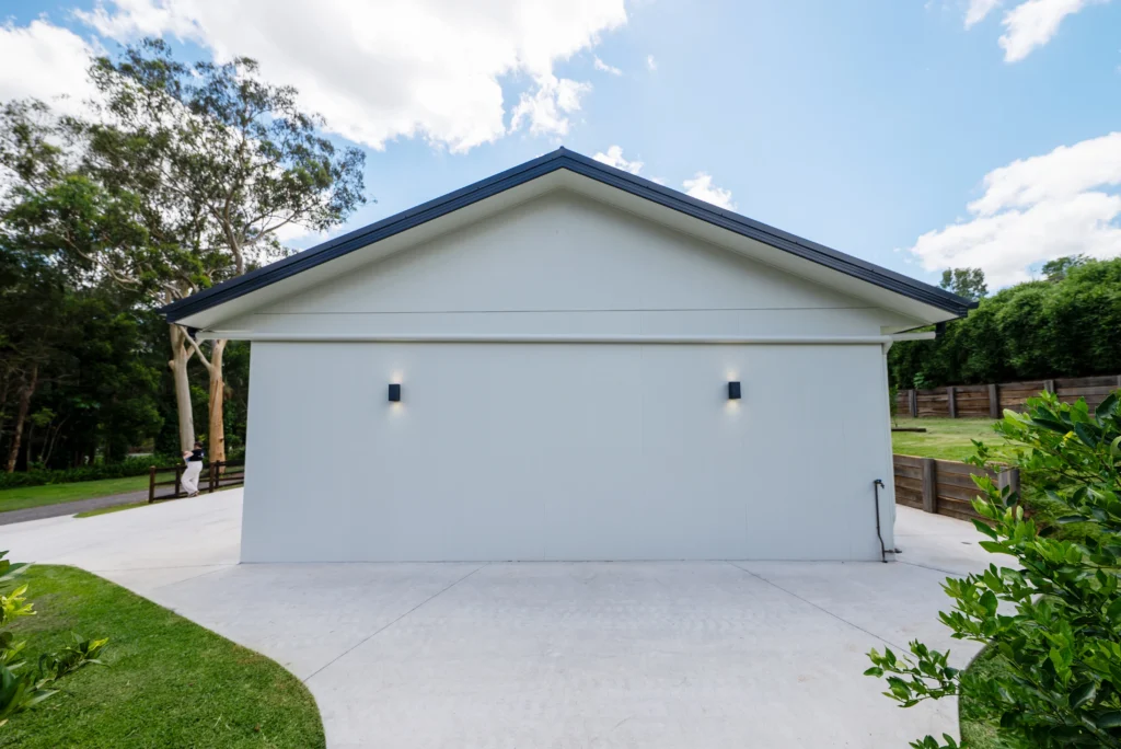 Custom rendered double garage with Colorbond roof, wall lighting and lush garden surrounds, Sunshine Coast by Bozcon Construct