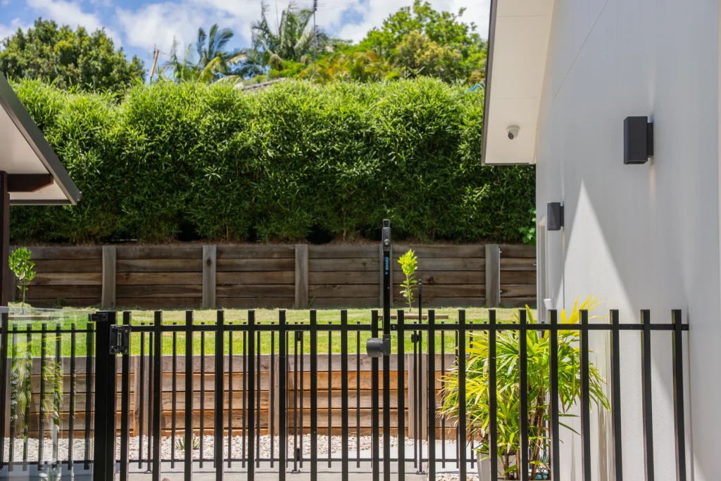 Outdoor entertaining area with black steel fencing, rendered feature wall and lush garden screening, Sunshine Coast by Bozcon Construct