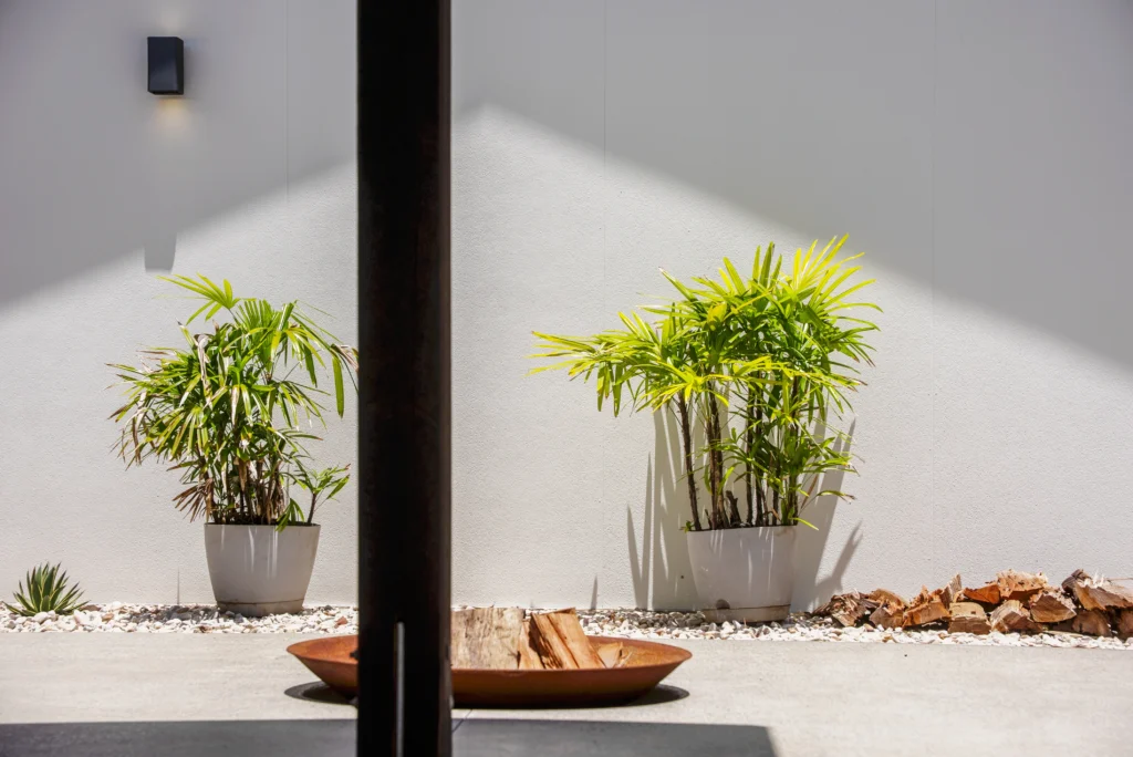 Outdoor entertaining area detail with rendered feature wall, tropical potted plants and fire bowl, Sunshine Coast by Bozcon Construct