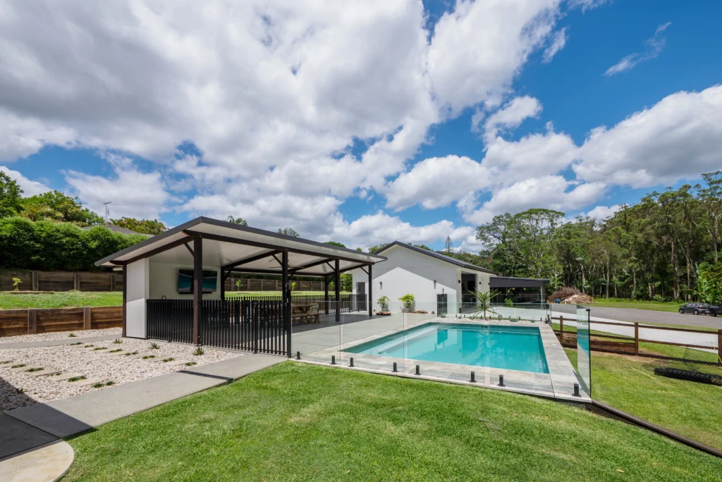 Completed outdoor entertaining area with in-ground pool, glass fencing, covered alfresco and lush lawn, Sunshine Coast by Bozcon Construct