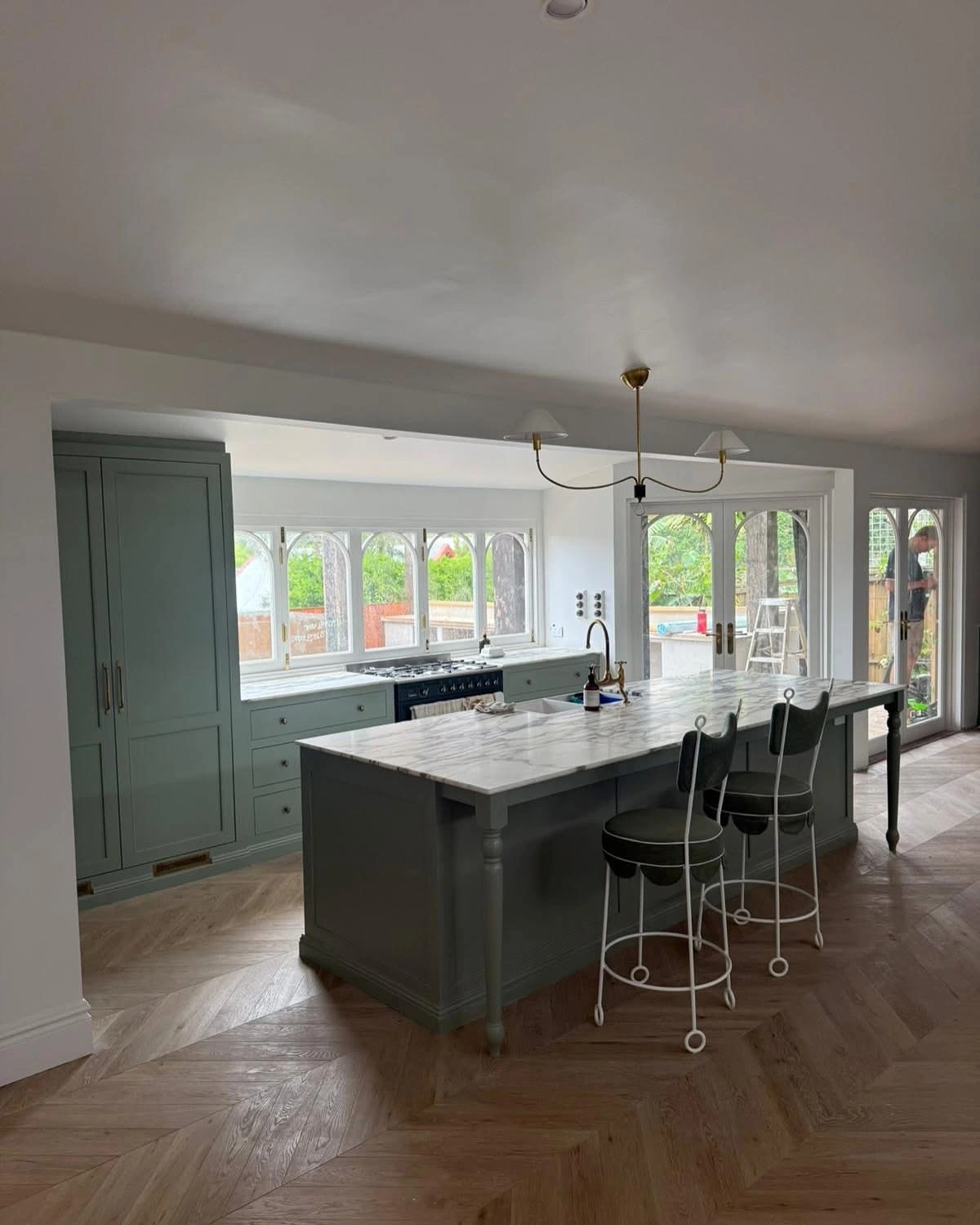 Renovated kitchen with sage green cabinetry, marble island bench and herringbone timber flooring at Sunrise Beach, Sunshine Coast by Bozcon Construct